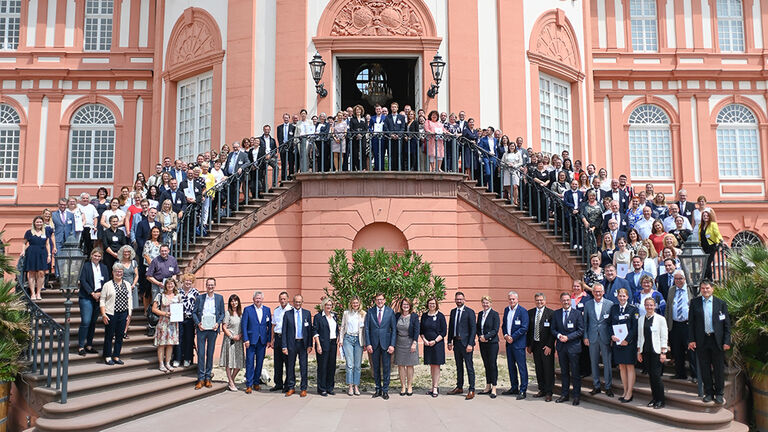 Gruppenfoto mit Vertreterinnen und Vertretern aller im Jahr 2022 mit dem Gütesiegel „Familienfreundlicher Arbeitgeber“ ausgezeichneten Dienststellen auf der Freitreppe von Schloss Biebrich