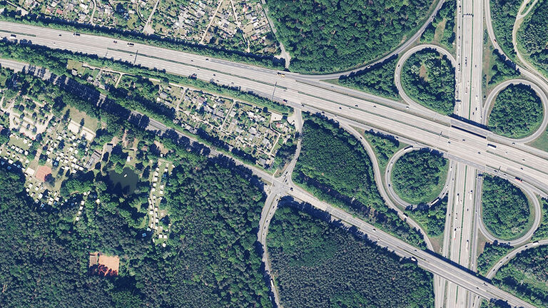 Luftaufnahme eines Autobahnkreuzes am Rand einer von Wald umgebenen Siedlung
