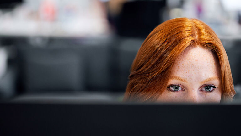 Frontalansicht von rothaariger junger Frau, die konzentriert auf einen Computermonitor schaut