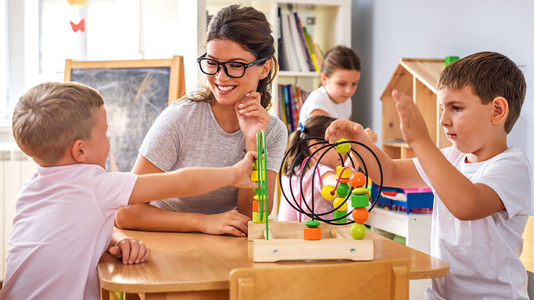 Erzieherin einer Kita, die mit zwei Kindern am Tisch sitzt 