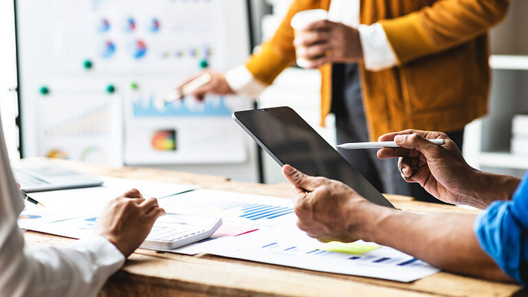 Blick in einen Konferenzraum mit drei Personen, die auf einem Flipchart und als Ausdrucke auf dem Tisch zu sehende Ergebnisse einer Business-Analyse besprechen