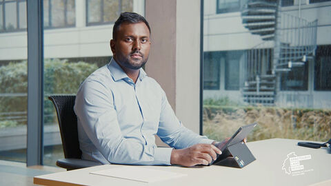 Werbebotschafter der Arbeitgeberkampagne des Landes Hessen: HZD-Mitarbeiter Surenthar Santhirasegaran HZD-Mitarbeiter sitzt mit Laptop am Schreibtisch und schaut in die Kamera