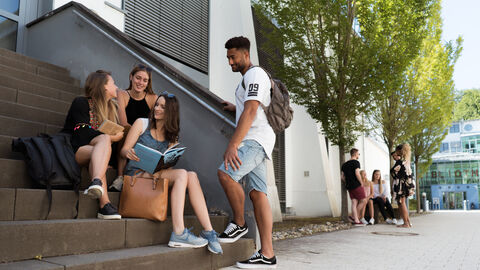 HZD-Partner beim dualen Studium: die Hochschule RheinMain Dual Studierende, die am Campus der Hochschule RheinMain auf einer Treppe sitzen