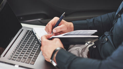 Bildausschnitt eines Mannes mit Notizbuch auf dem Schoß, in das er schreibt