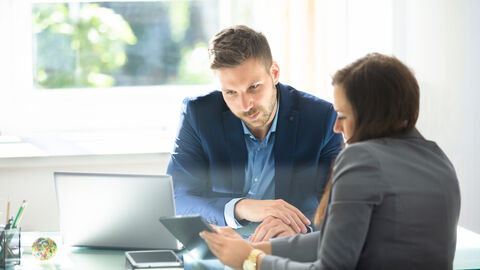 Frau und Mann am Konferenztisch im konzentrierten Gespräch mit Blick auf einen Laptop