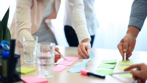 Konferenztisch, auf dem drei Menschen mit farbigen Klebezetteln ein Projekt planen 