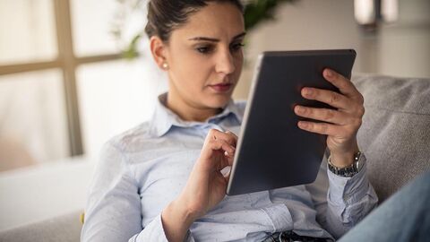 Spannende Lektüre rund um das Thema IT – das HZD-Kundenmagazin INFORM Frau in heller Bluse, die auf einem Sofa sitzend einen Text auf ihrem E-Reader liest