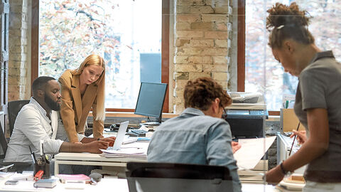 Blick in zeitgemäßes Büro mit vier jungen Menschen in Arbeitsgesprächen