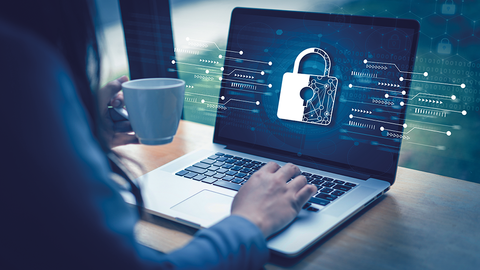 Blick auf Schreibtisch mit Laptop und darüber gelegter Grafik aus Vorhängeschloss und Schaltplänen