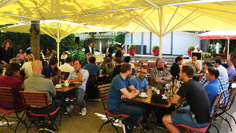 Gäste des D-Talk 2022 in Hünfeld, die unter gelben Sonnenschirmen in einen Biergarten sitzen