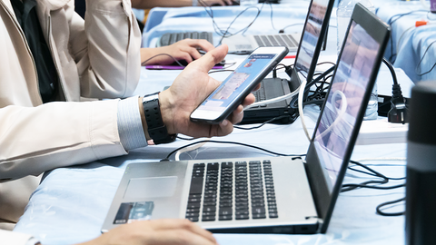 Offene Türen für IT-Interessierte beim Schul- und Hochschulpartner HZD Close-up auf Tischreihe mit offenen Laptops und angedockten Smartphones, an denen Lernende arbeiten