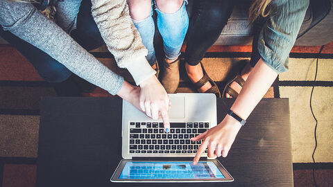 Blick von oben auf drei Personen vor einem niedrigen Tisch, die gemeinsam an einem Laptop arbeiten