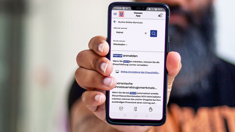 Digitale Verwaltung aus kundiger Hand: die von der HZD entwickelte HessenApp Mann mit Handy in der weit vorgestreckten Hand; auf dem Display ist die Benutzeroberfläche der von der HZD entwickelten HessenApp zu sehen
