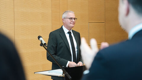 Joachim Kaiser wird von Vertreterinnen und Vertretern der Landesverwaltung mit Standing Ovations verabschiedet. HZD-Direktor Joachim Kaiser steht an einem Stehpult vor einem applaudierenden Publikum