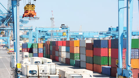 Hafenansicht mit aufeinander gestapelten bunten Containern und einem verzweigten System aus Schienenbrücken und Verladekränen