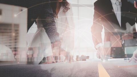 Menschen in Anzügen und Jacketts, die mit den Händen auf einen Tisch stützen. Das Bild ist überlagert von gestapelten Transport-Containern und hellen Lichtpunkten