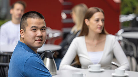 Beste Voraussetzungen für eine aussichtsreiche Karriere – mit dem Informatik-Stipendium der HZD Junger Mann, der im Innenhof der HZD in einer Gesprächsrunde am Tisch sitzt und über die Schulter in die Kamera blickt