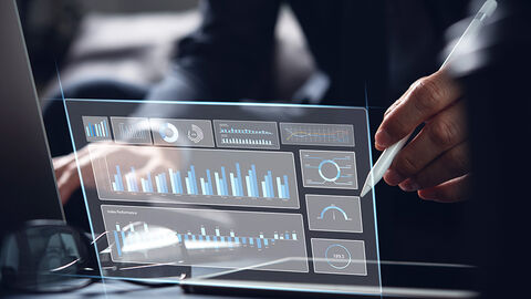Top-Noten in Sachen Marktpositionierung: das HZD-Benchmarking 2023 Close-up auf Schreibtisch, auf den das Hologramm eines Monitors mit unterschiedlichen Grafiken zur Leistungsdarstellung projiziert ist
