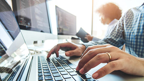 Bürosituation mit Close-up auf die Hände eines Mannes, der die Tastatur eines Notebooks bedient