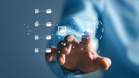 Close-up auf nach vorn ausgestreckte Hand, deren Zeigefinger auf darübergelegte Grafik mit symbolisiertem Sicherheitszertifikat tippt