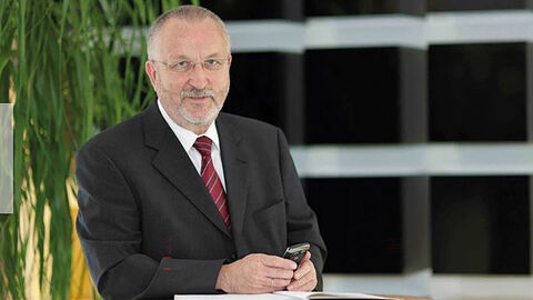 Herbert Guder Mann im Anzug steht angelehnt an Tisch und hält Handy in Hand.