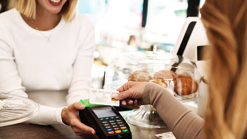 Close-up auf die Theke eines Cafés, auf der die Servicekraft einem weiblichen Gast das Gerät zum Bezahlen per Karte hinhält