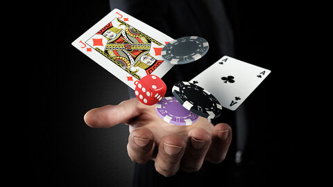 Ausgestreckte Männerhand, die vor einem dunklen Hintergrund Spielkarten, Spielchips und Würfel in die Luft wirft