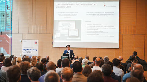 Ein Mann mit Mikrofon vor Publikum im Konferenzsaal