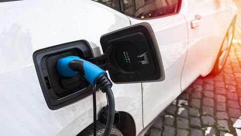 Close-up auf Ladepunkt eines weißen Autos, in dem ein blaues Ladekabel steckt