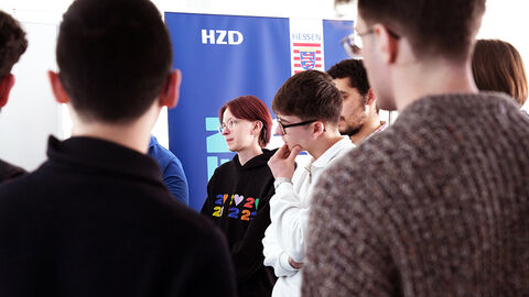 Halbtotale einer Gruppe von Studierenden, die vor einer HZD-Flagge stehend ins Gespräch vertieft sind